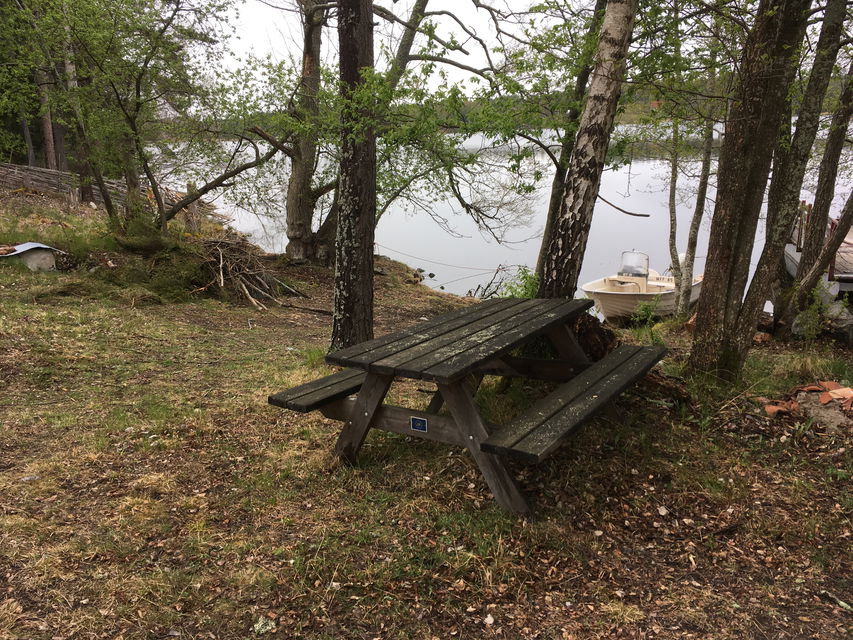 Ett bänkbord står på en öppen yta vid vattnet. Från rastplatsen är det nära till båtbryggan.