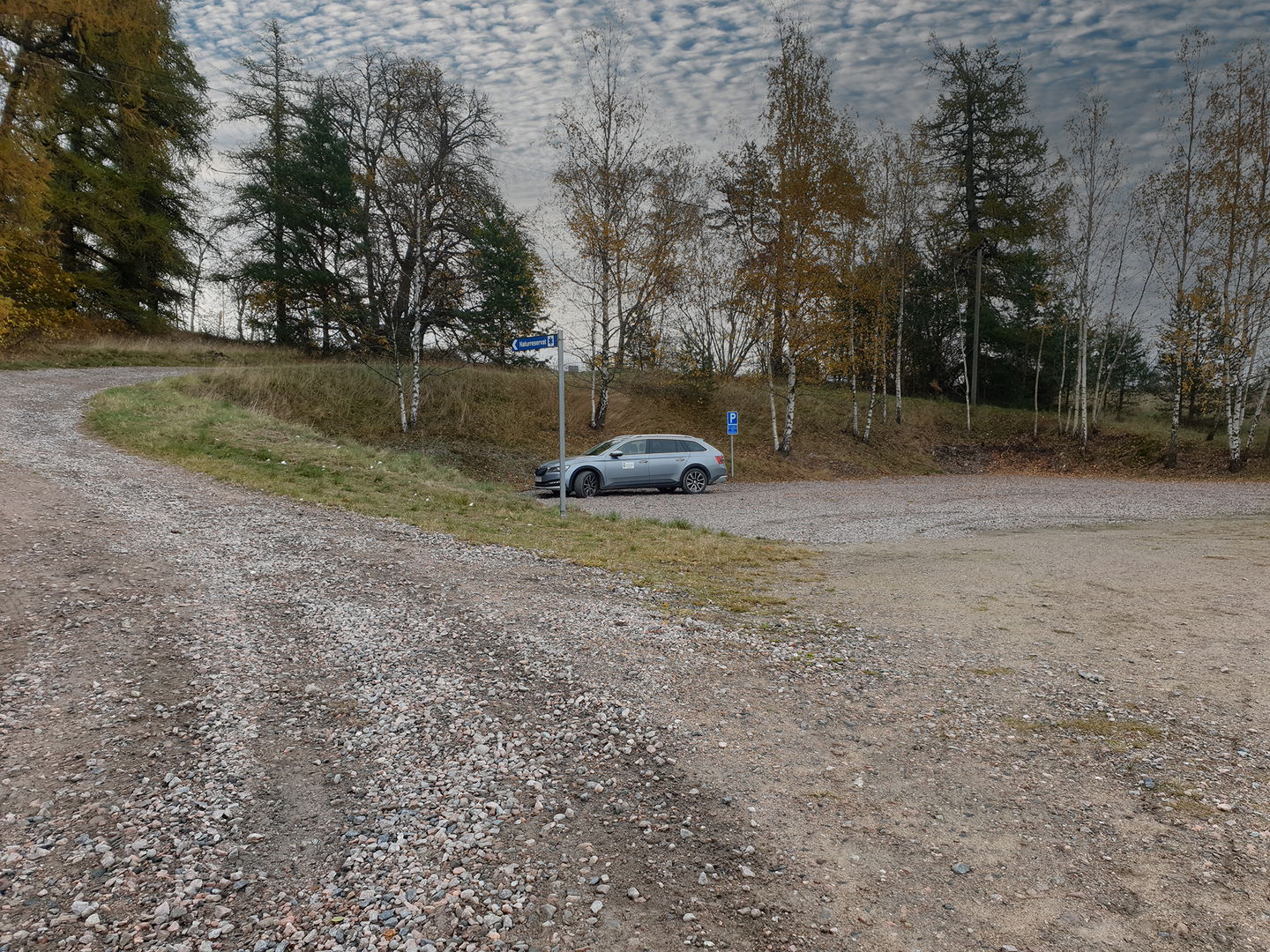 En silverfärgad kombi står på en grusad yta vid en parkeringsskylt.