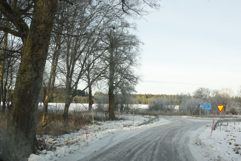 En smal ficka vid bilvägen med en busshållsplats-skylt. Bortanför hållplatsen är det en vägkorsning.