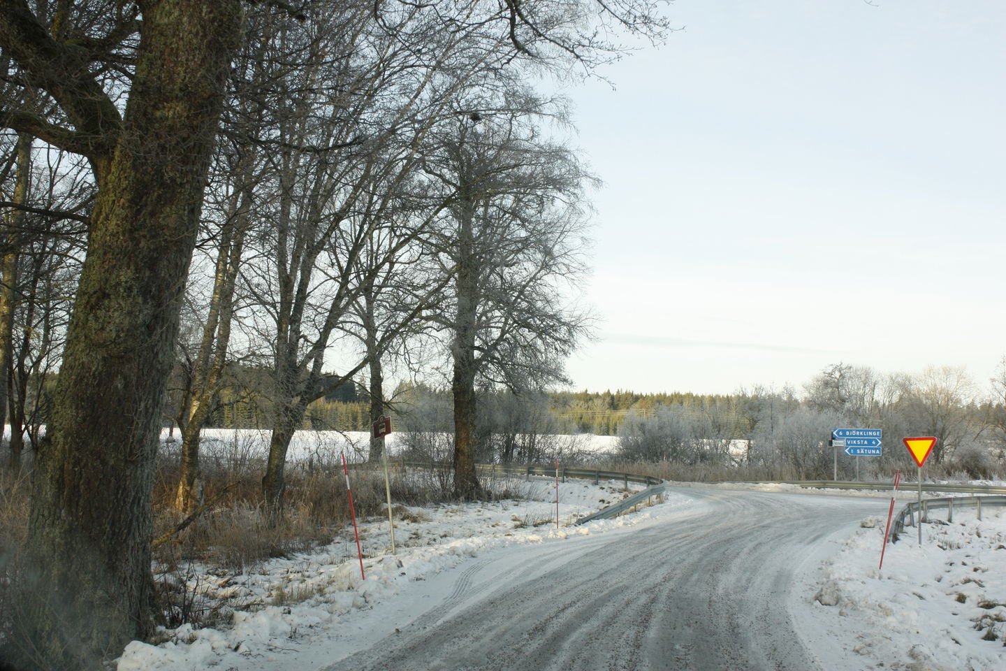 En smal ficka vid bilvägen med en busshållsplats-skylt. Bortanför hållplatsen är det en vägkorsning.
