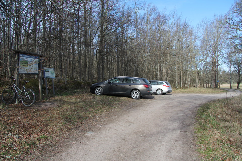 Två bilar står parkerade på parkeringen. Det finns en informationstavla över naturreservatet. Mot den står en cykel lutad.