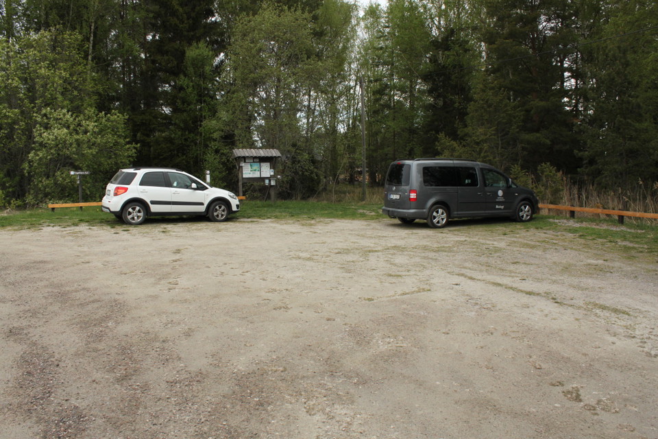 Två bilar står på en stor parkeringsplats. Bredvid parkeringen finns en infromationsskylt.