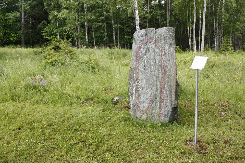 En runsten står på gräsmark med en informationsskylt bredvid.