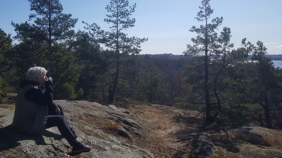Kvinna som sitter och dricker kaffe på en bergknalle med skog och Lilla Värtan