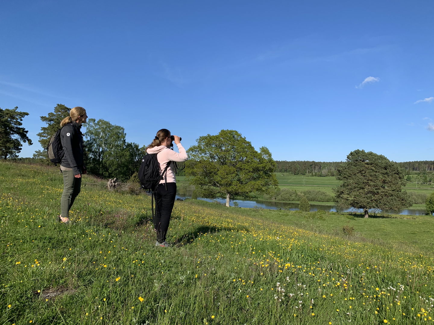 Två kvinnor står i en sluttning. En av kvinnorna tittar i en kikare.