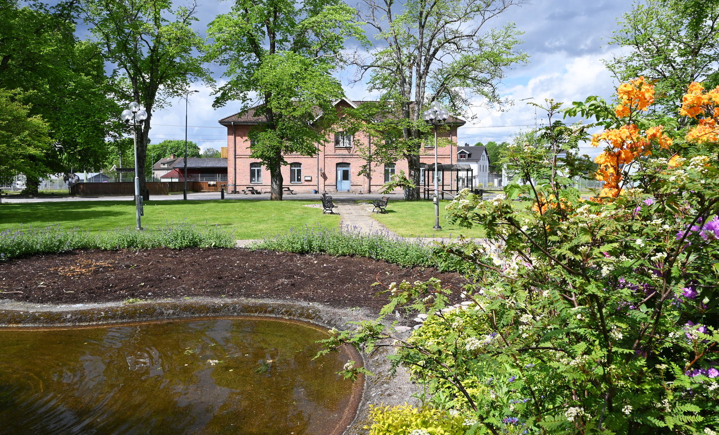 Planteringar, damm, grönyta, gammalt stationshus.