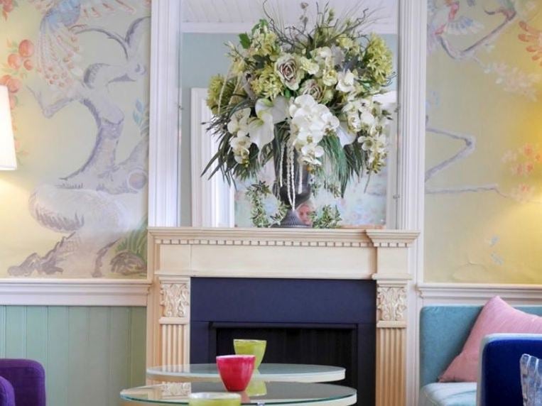 Ett rum med en öppen spis och en öppen spis och en vas med blommor.
