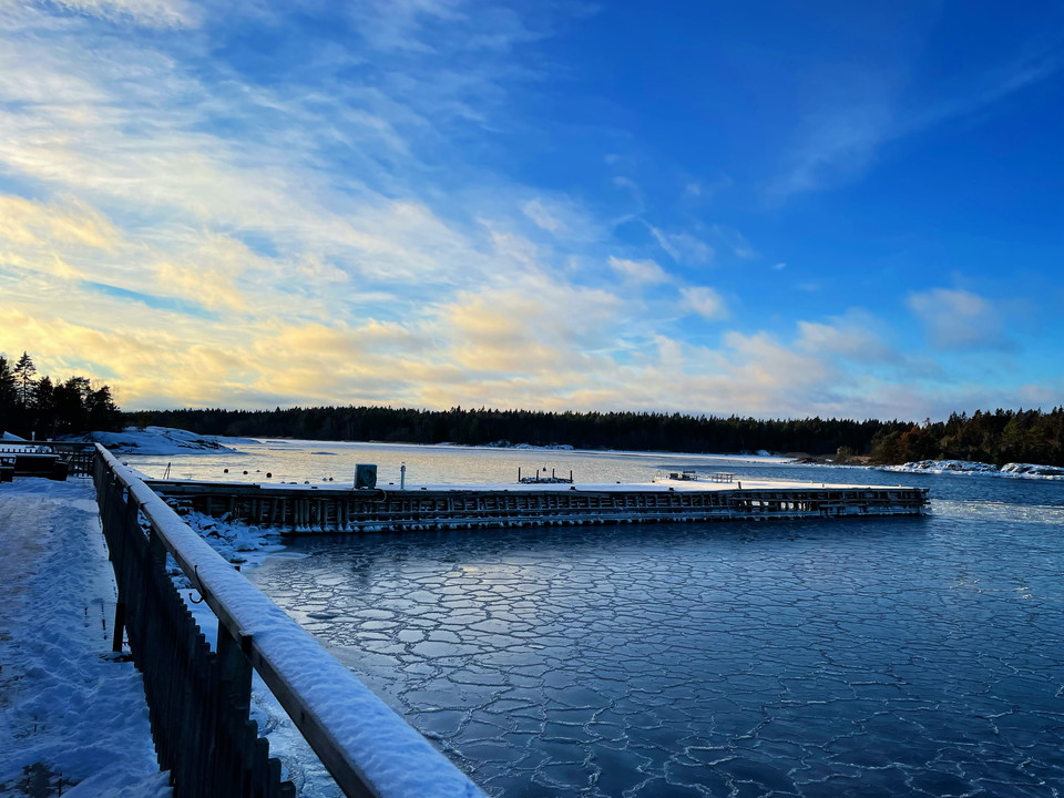Ett snöklätt räcke längs ett trädäck vid havet.