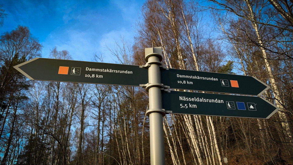 Skyltar till vandringsleder med blå himmel och träd i bakgrunden.