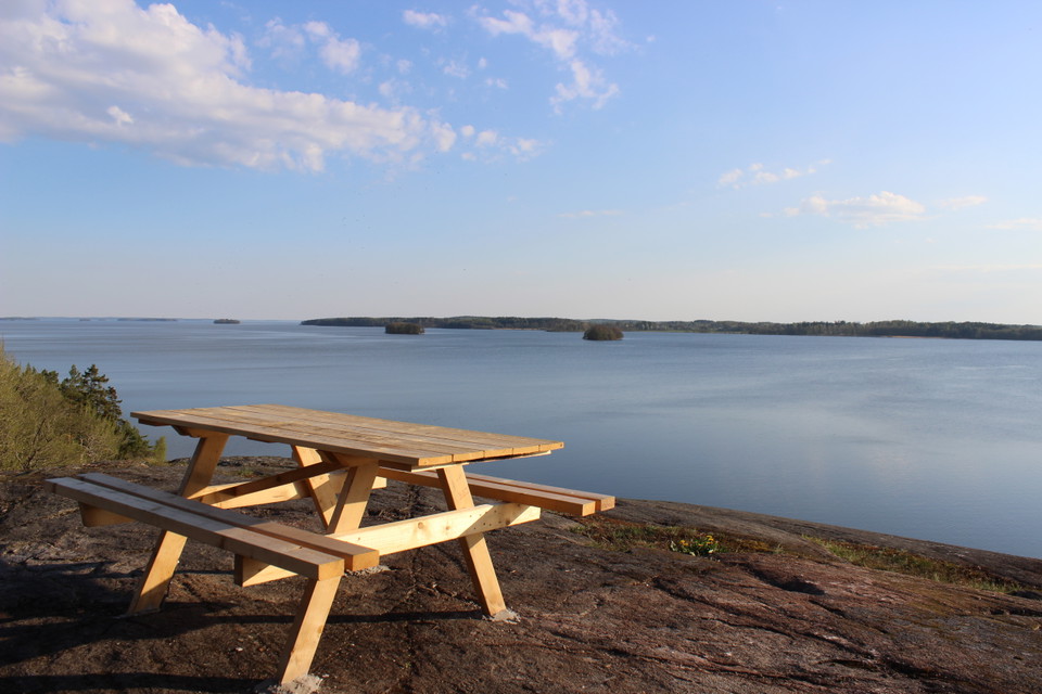 Ett bänkbord står på höga klippor med utsikt över vatten och öar.