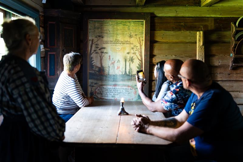 Besøkende som sitter rundt ett bord, mens museumsverten forteller fra gamle dager.
