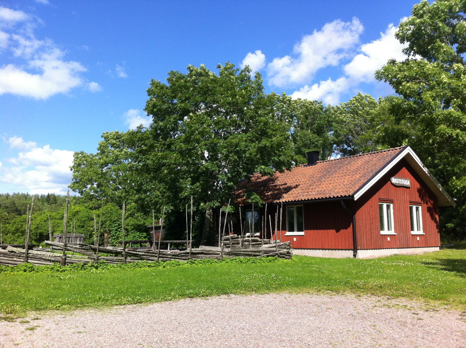 Ett grusplan leder fram till en stuga med en gärdesgård bredvid.