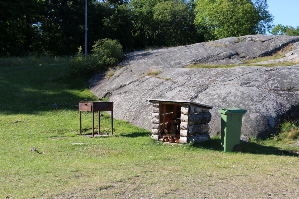 Grill, vedförråd och soptunna intill klipphäll.