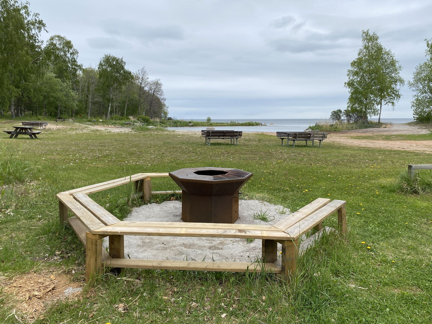 Grill med bänkar runt om på en gräsmatta med utsikt över badplats