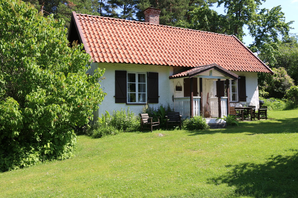 Ett vitt torp med en välklippt gräsmatta och en stor syrenbuske på ena sida.