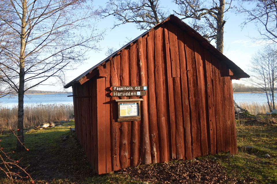 På baksidan av en äldre bod av trä sitter en karta och pilar mot fågeltornet och harudden. I bakgrunden syns havet.
