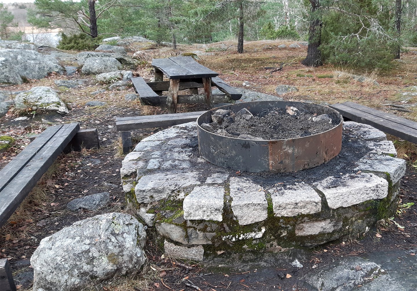 En grillstad i sten och metall kantad av tre träbänkar.