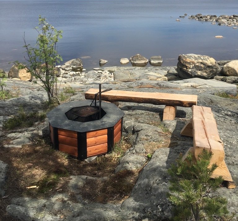 En låg grillplats med två sittbänkar står på en stenhäll vid havet.