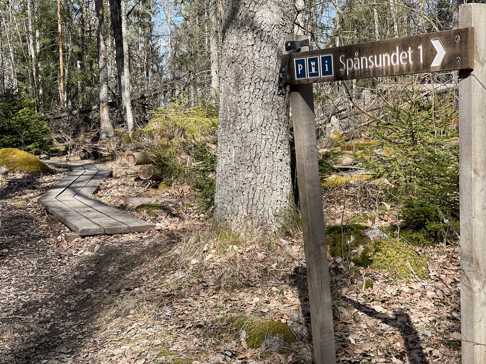 Stig med spång och en pil som visar riktning mot parkering och toalett.