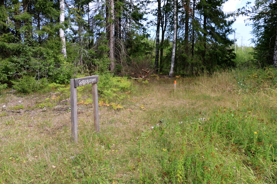 Vägvisningsskylt och knähög trästolpe med orange topp-