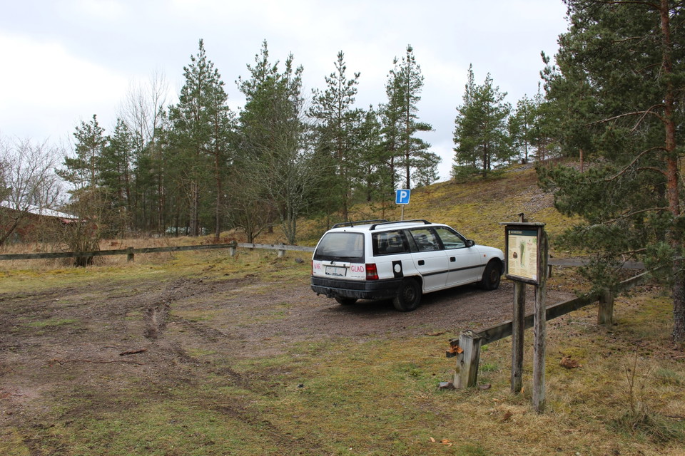En bil står parkerad på en markerad parkeringsplats med en informationsskylt. Marken lutar något och är ganska lerig.