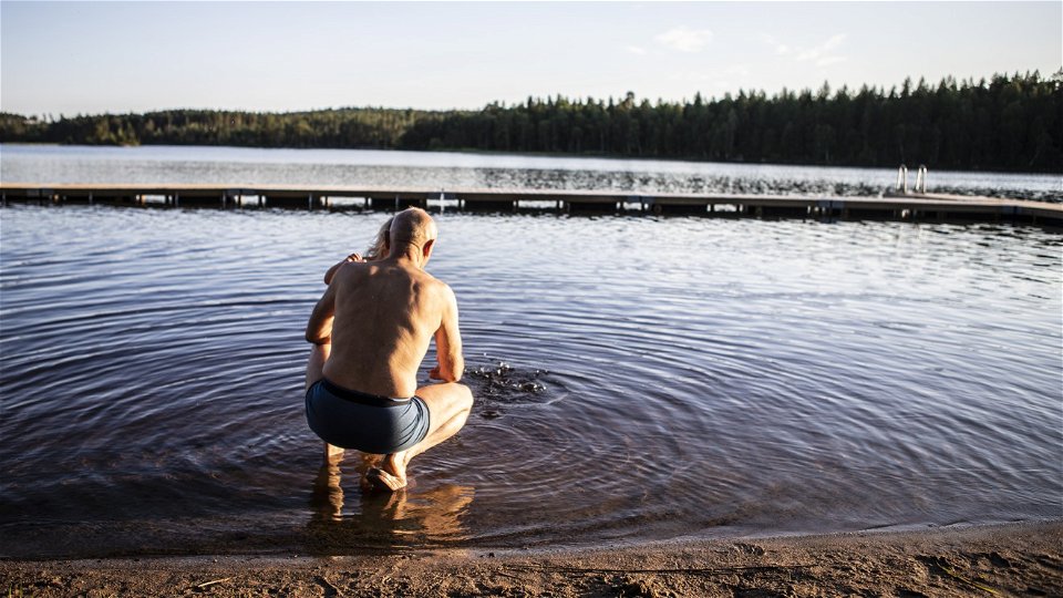 En man sitter på huk med ett barn och tittar ut över en sjö