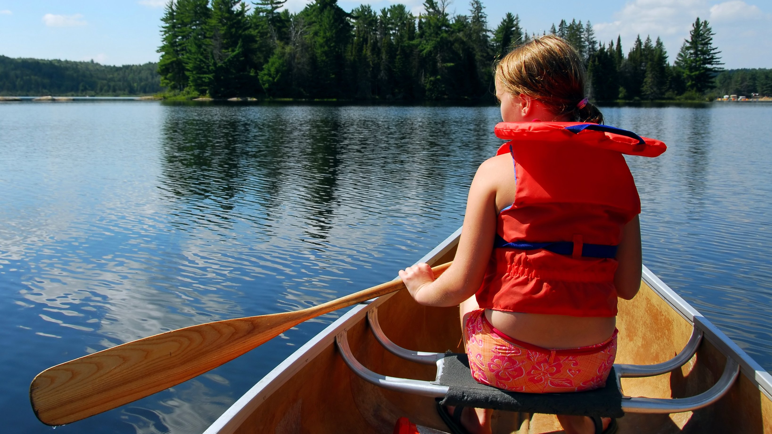 En flicka med flytväst i en kanot i en sjö.