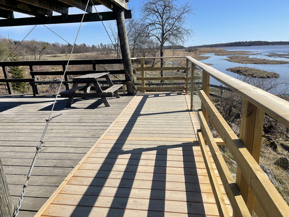 Våningsplan på utsiktstorn. Del av staket har plexiglas. Ett picknickbord står vid staketet.