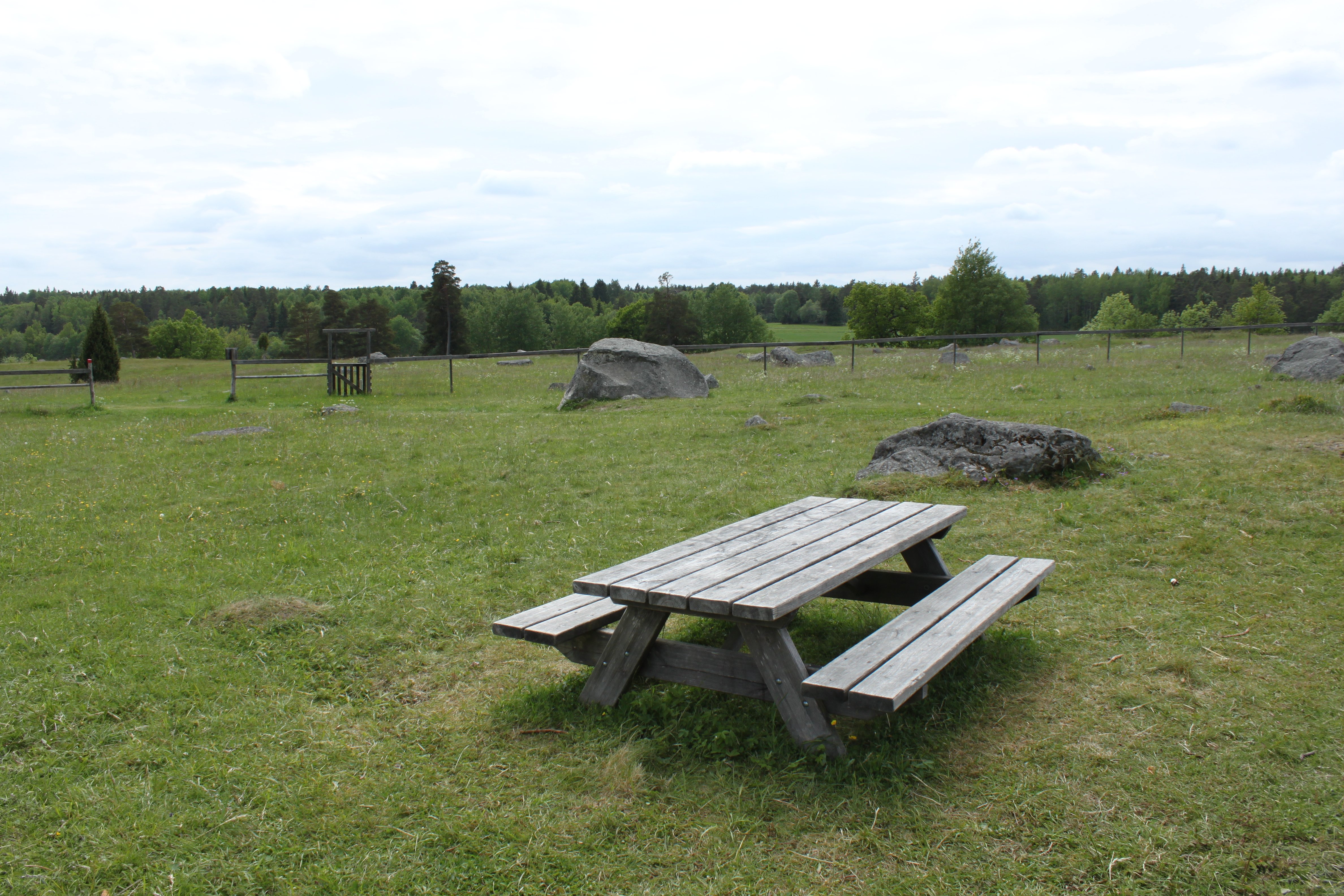 Ett bänkbord står på en öppen gräsyta med flera större stenblock i bakgrunden.