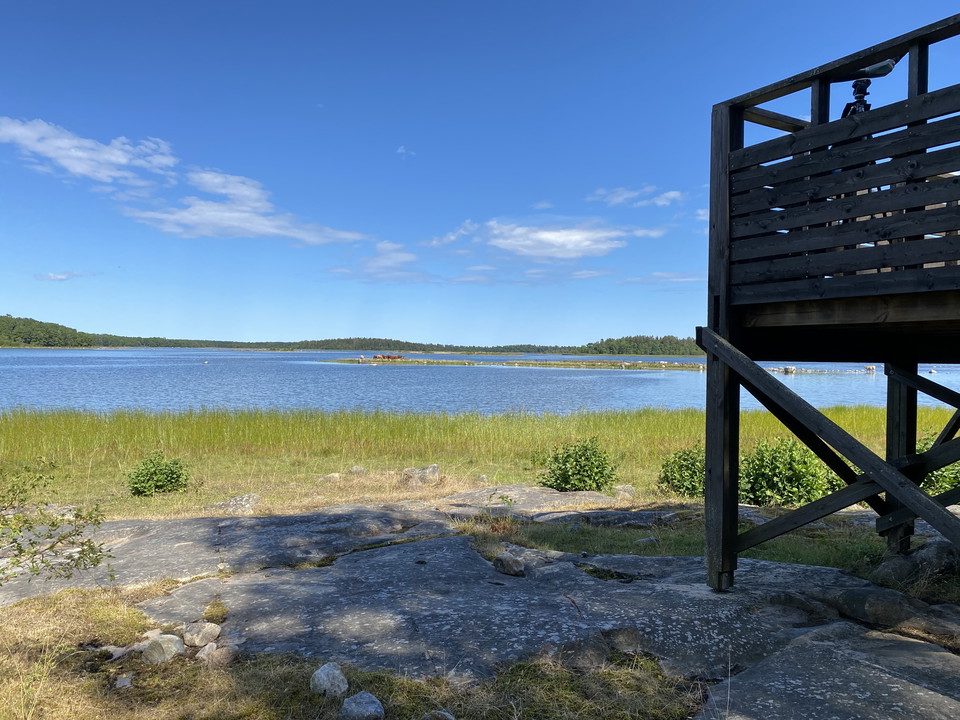 Ett fågeltorn står på en klippa vid vattnet. Halva tornet syns på bilden.