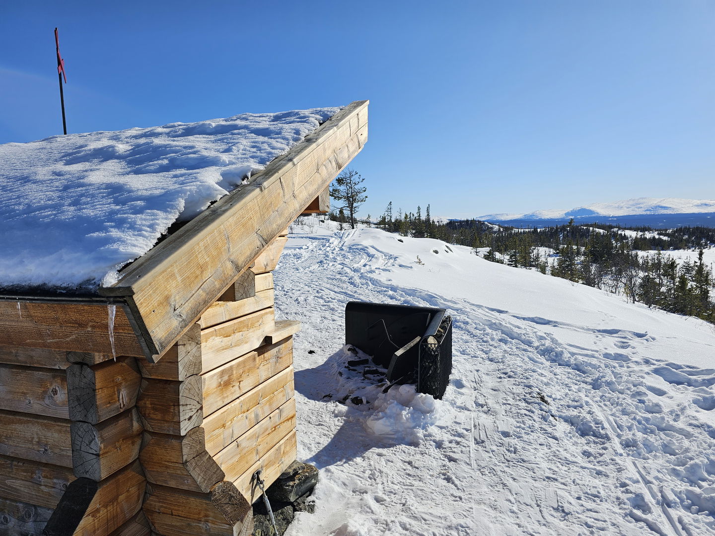 Ett timrat vindskydd med en eldstad framför och utsikt mot fjäll.