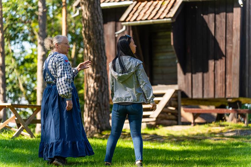 Museumsverten og en besøkende står og beundrer de gamle bygningene.