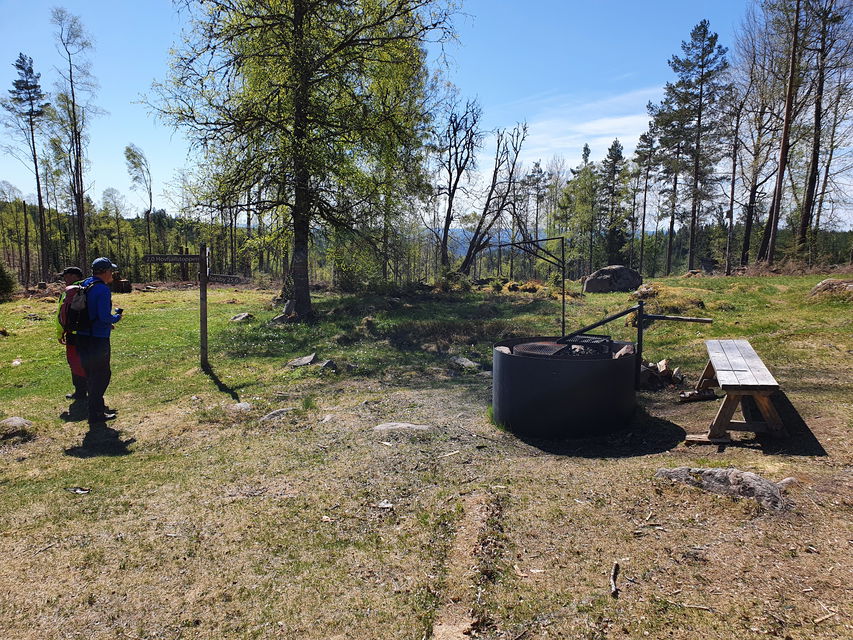 Eldplats med bänk intill samt två personer en solig dag.