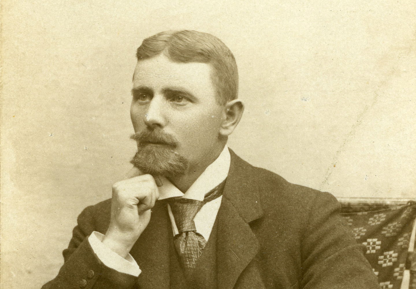 Porträtt av unge Gotthard Nilsson sittande i en stol med hakan i handen. Han har kammad mittbena, slips och väst med kavaj.