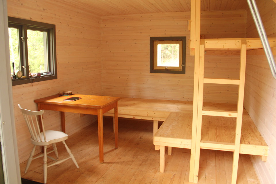 Inne i stugan: stol, bord, två britsar och en överslaf