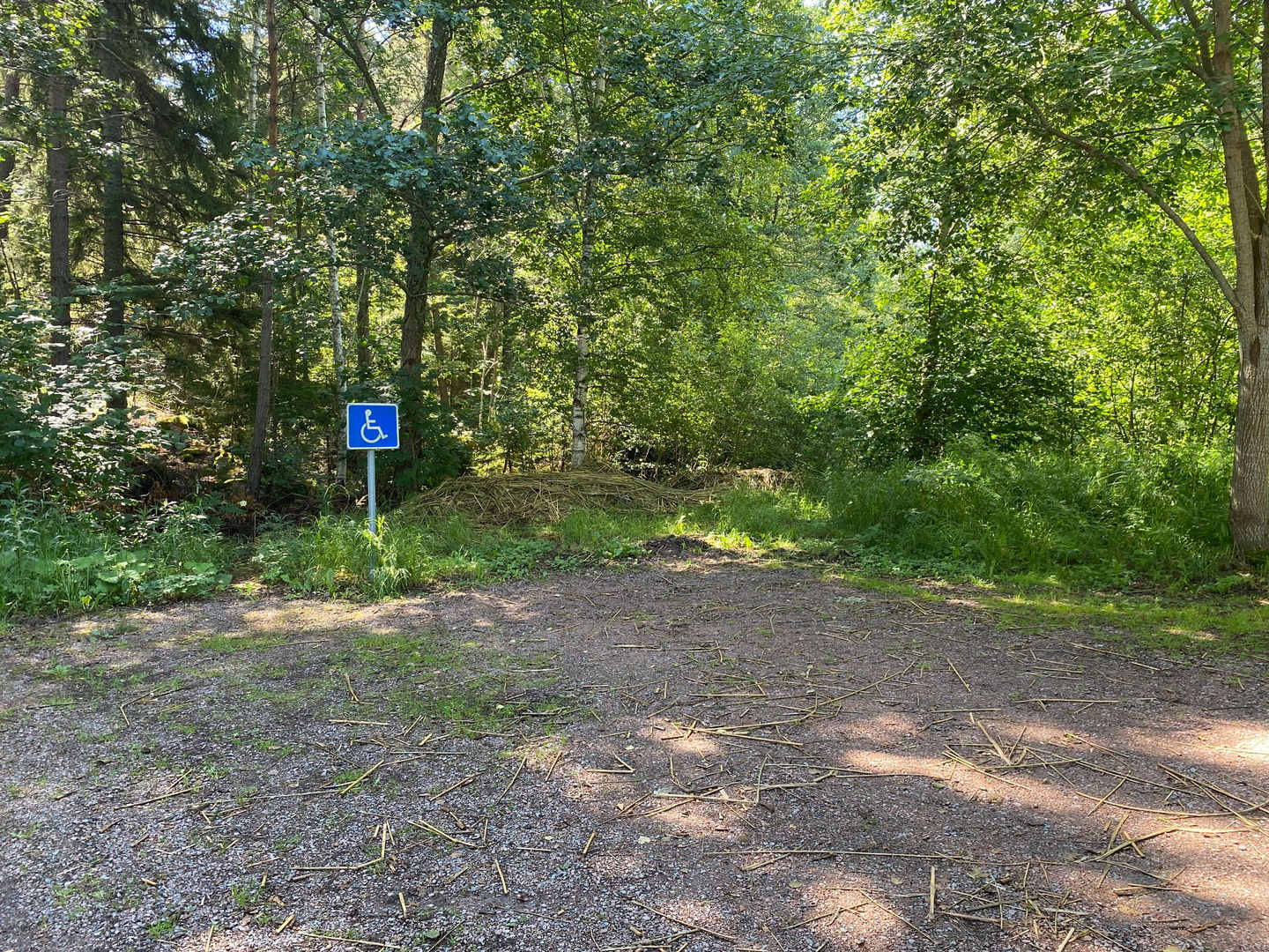 En skylt för handikapparkering står på en liten grusad parkeringsplats med skog runtom.