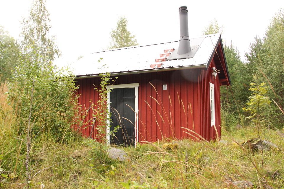 Liten röd stuga med svart dörr.