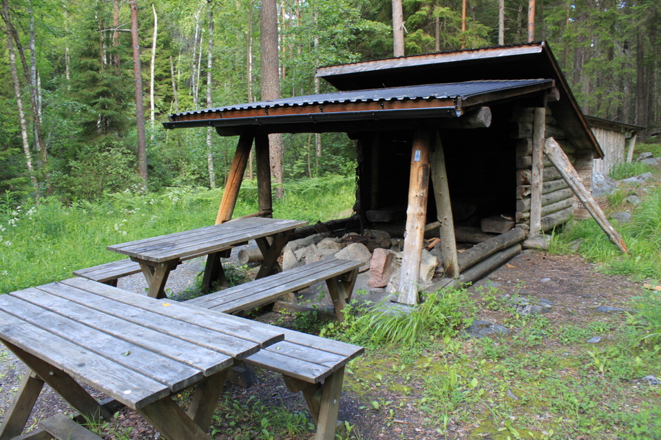 Närbild på bänkbord och vindskyddet. Framför vindskyddet finns en eldplats med tak över.