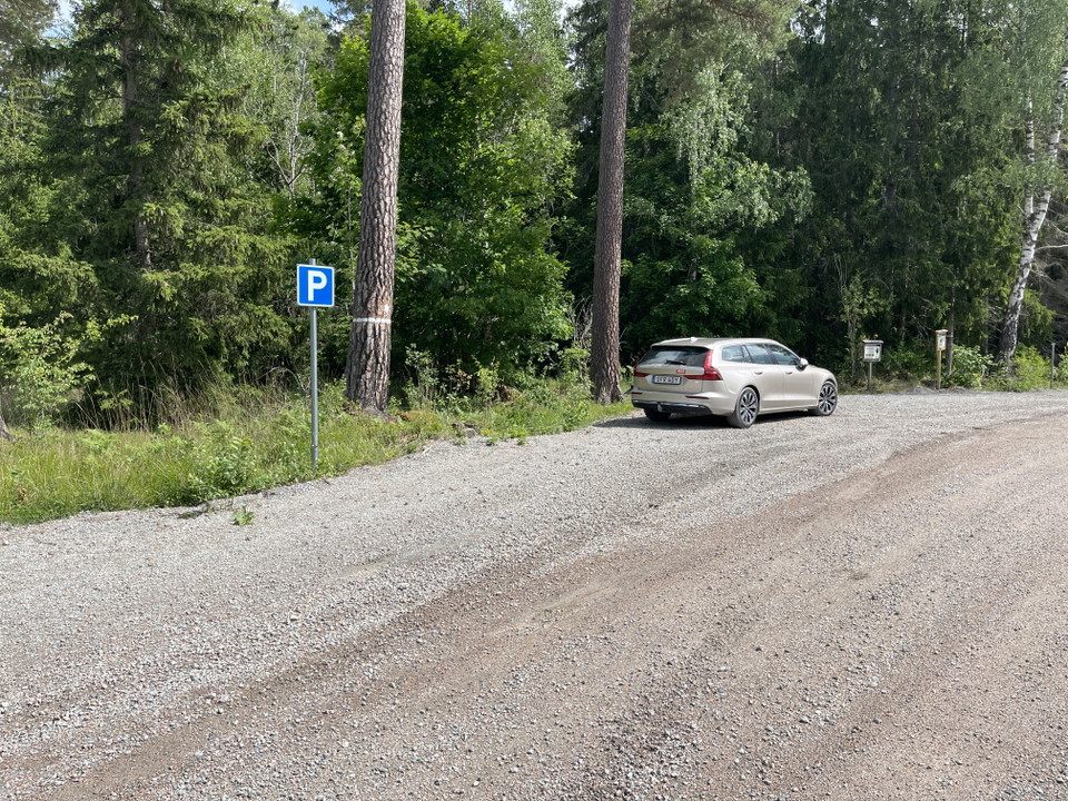Bil parkerad på en grusad yta vid grusväg. En p-skylt.