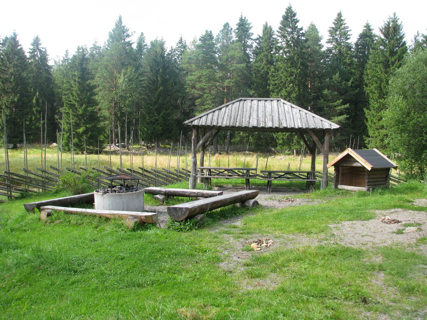 Sittbänkar, grillplats, vedförråd och takskydd intill en hage