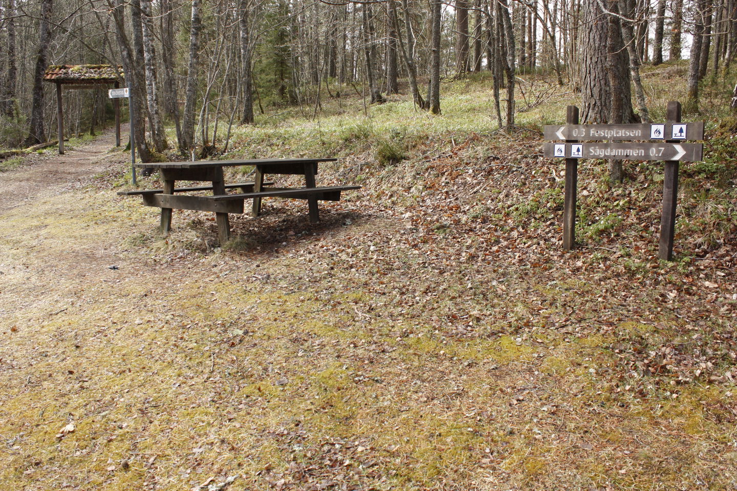 Ett bänkbord står i naturen. Bredvid rastplatsen finns en vägvisare. 