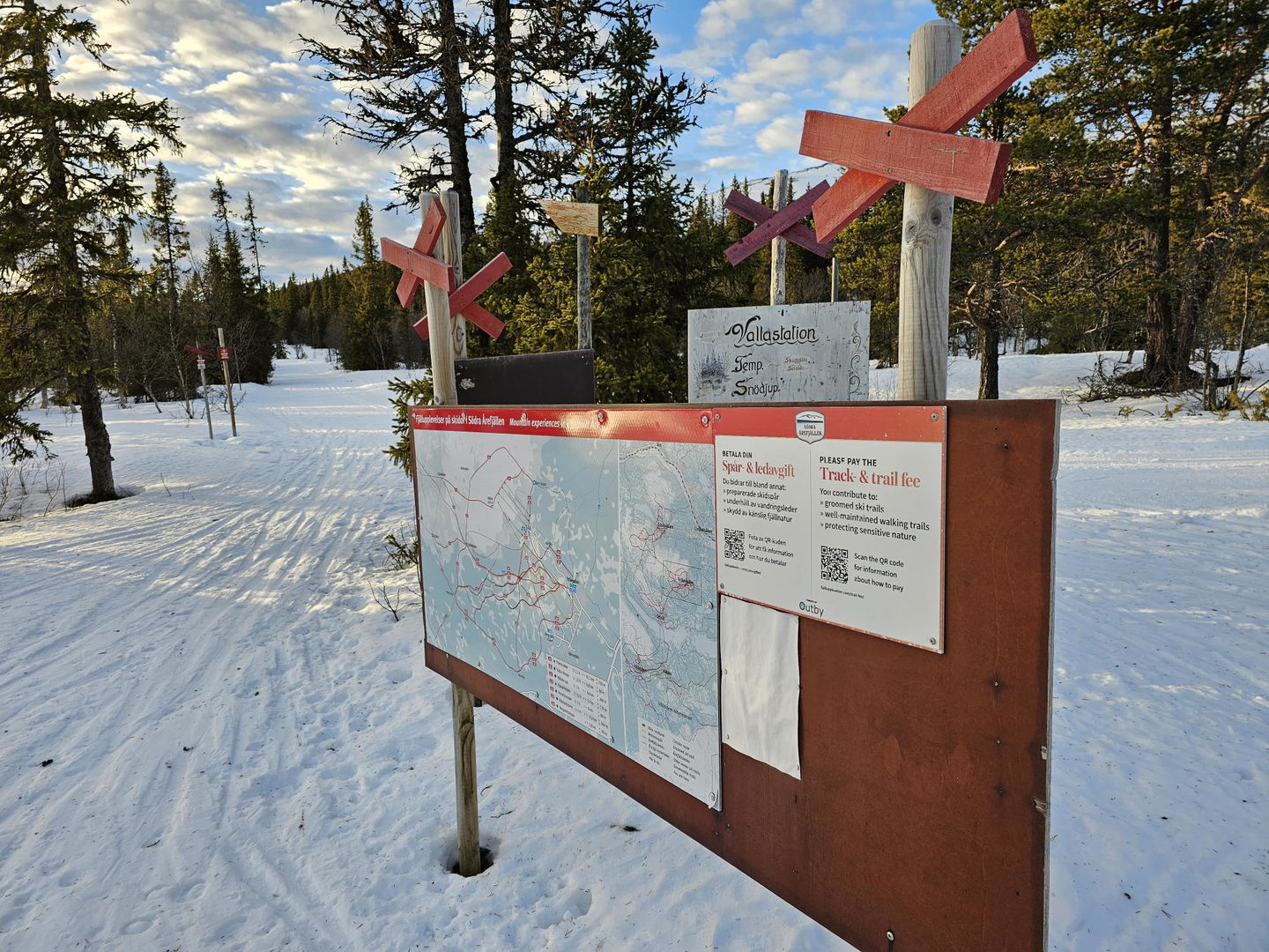 Spårkarta på en skylt med skog omkring samt ledkryss i bakgrunden