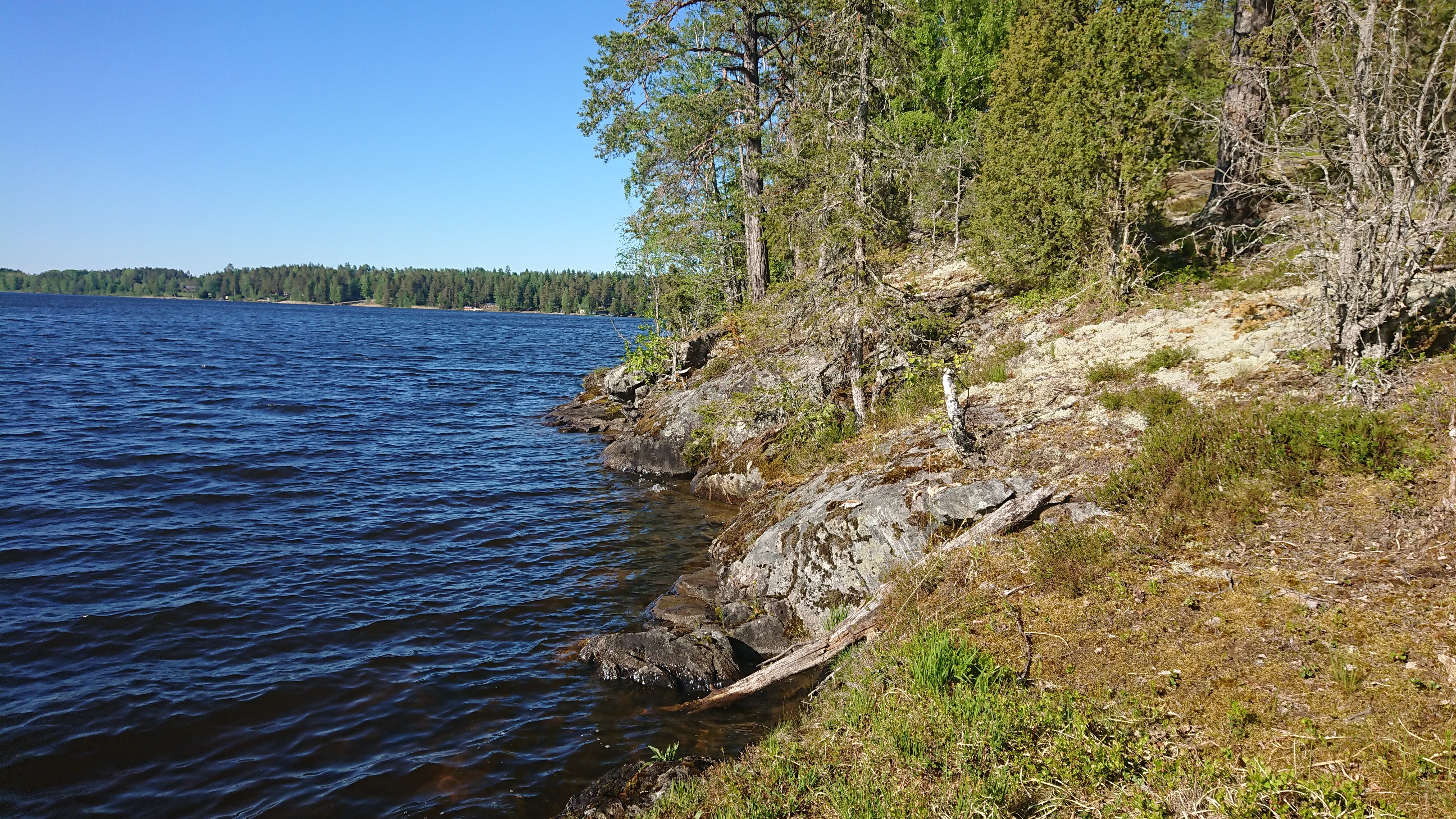 En sjö till vänster, till höger klippor som går ner i vattnet och lite skog.