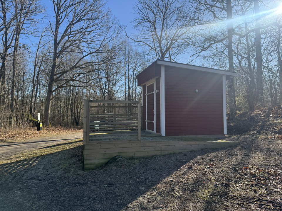 Ett rött litet trähus med utedass vid Delary badplats.