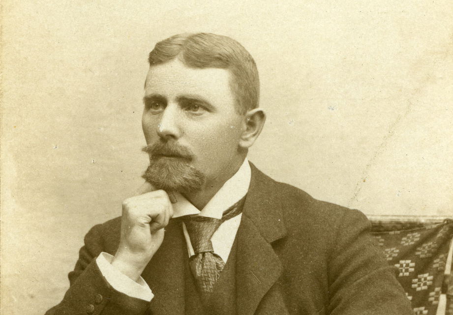 Unge Gotthard Nilsson sittande i en stol med hakan i handen. Han har kammad mittbena, slips och väst med kavaj.