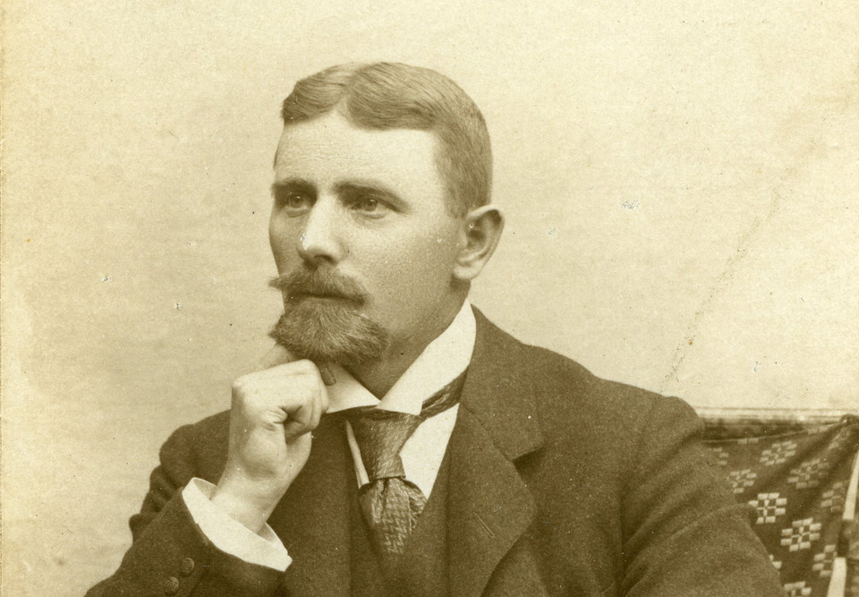 Unge Gotthard Nilsson sittande i en stol med hakan i handen. Han har kammad mittbena, slips och väst med kavaj.