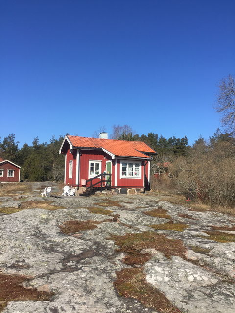 På en ojämn bergshäll står ett litet hus. En trappa med handräcken leder upp till dörren. 