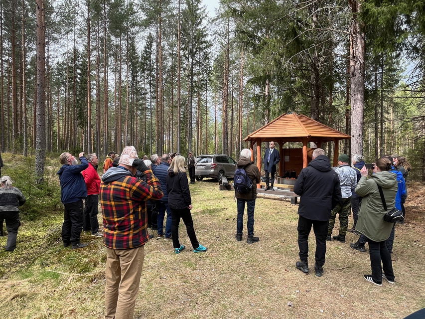 Ett 20-tal personer står runt en grillplats med tak.