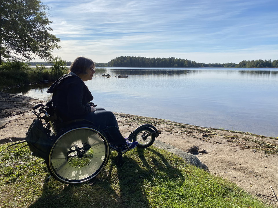 En kvinna som sitter i rullstol tittar ut över vattnet och stranden