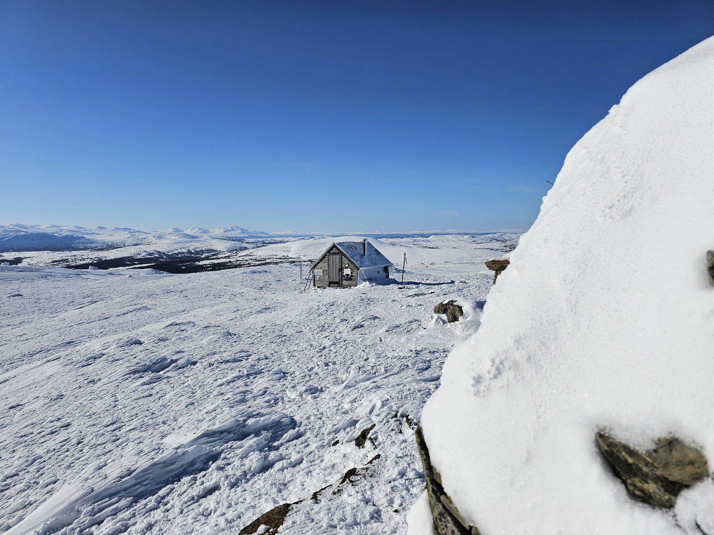 Liten stuga sedd på håll bakom en sten i snöig miljö